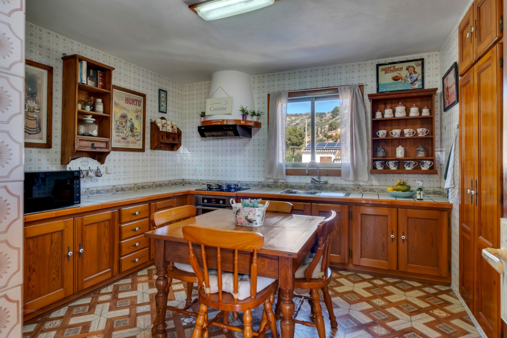 Rustic-style kitchen featuring solid wooden cabinetry, a central dining area, and patterned ceramic tiles. A window provides natural light and views of the hills.