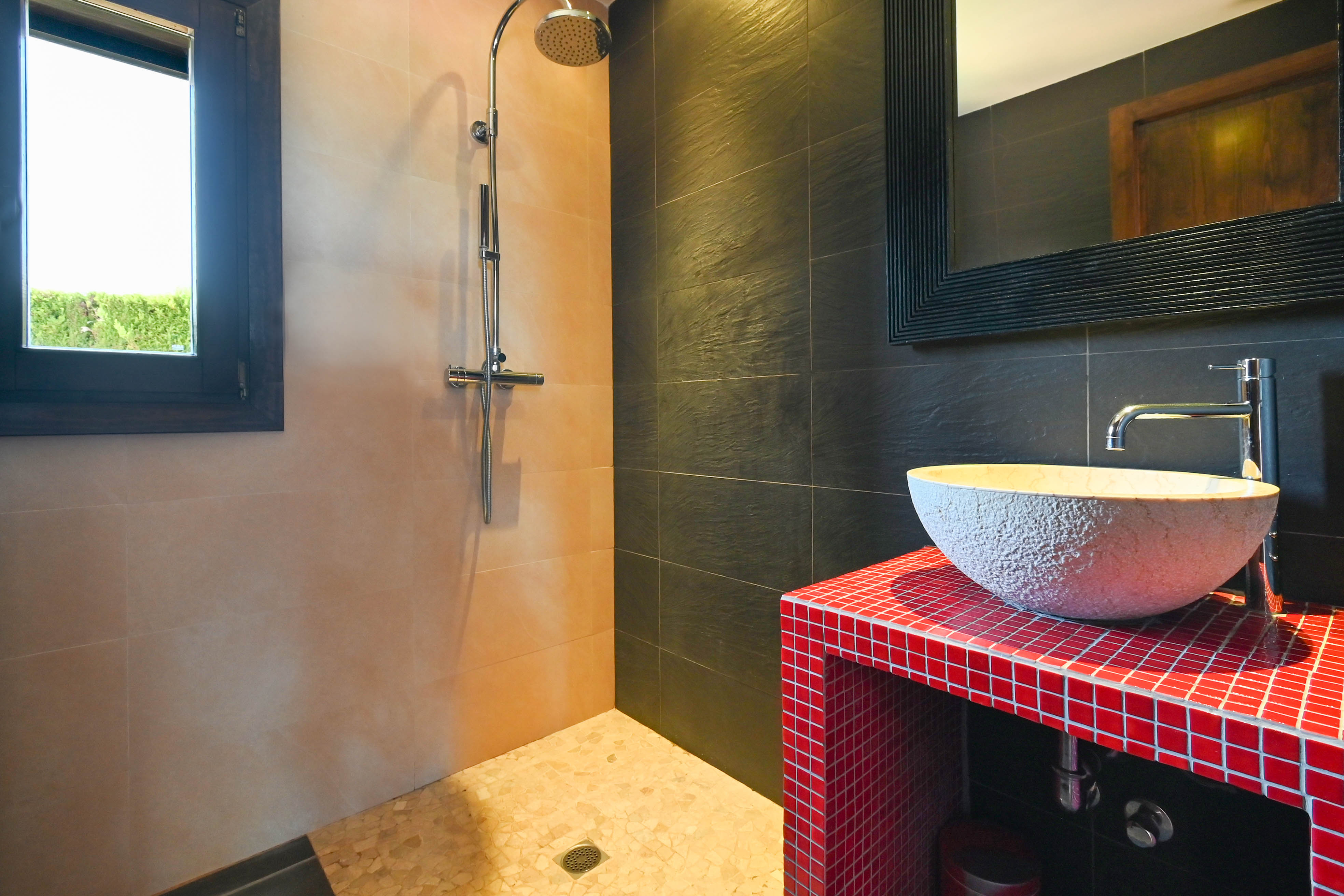 Bathroom detail with rustic sink on red mosaic countertop and shower with sand-colored tiles.