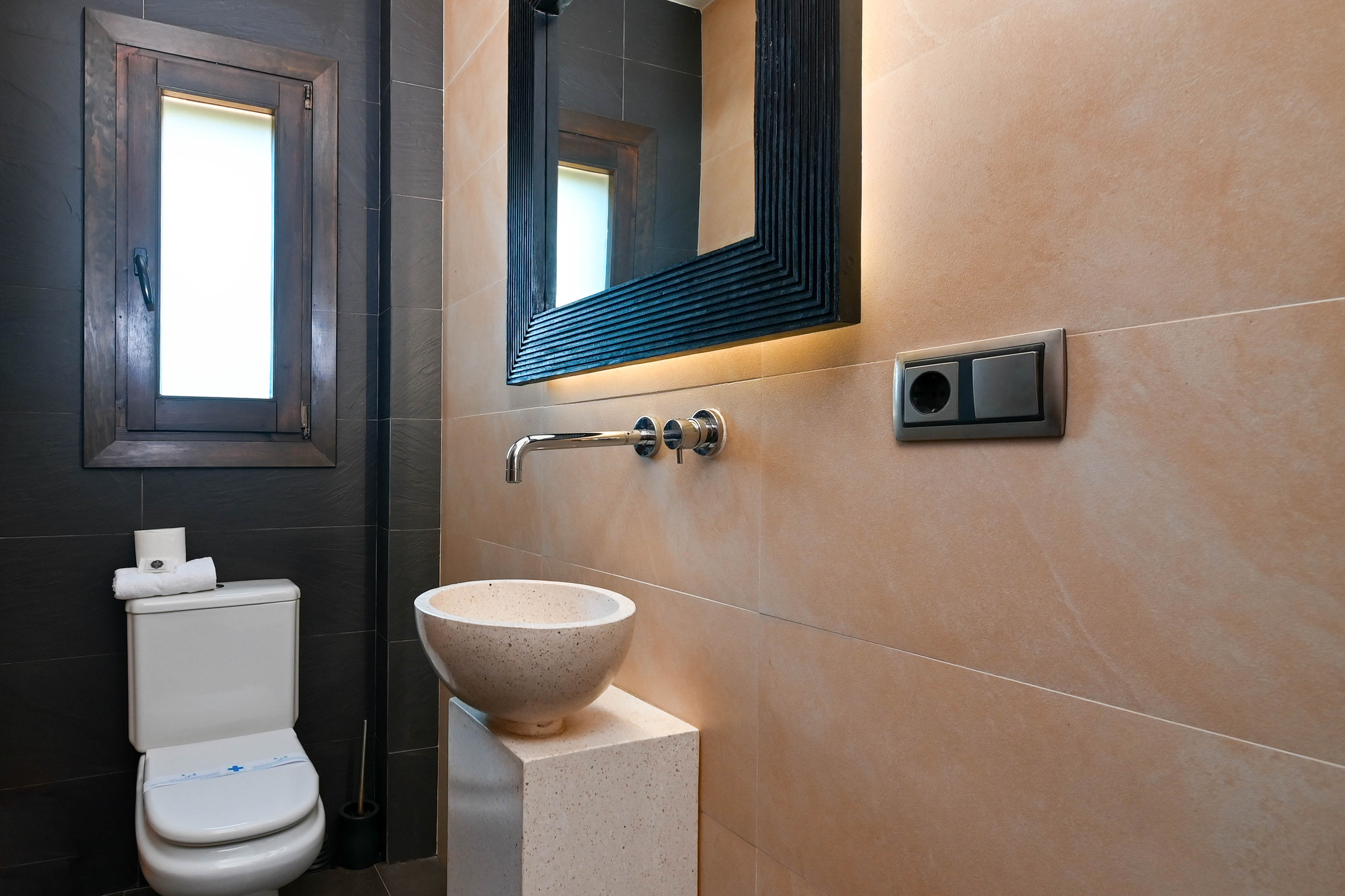 Bathroom detail with stone sink on a pedestal and a mirror with integrated lighting.