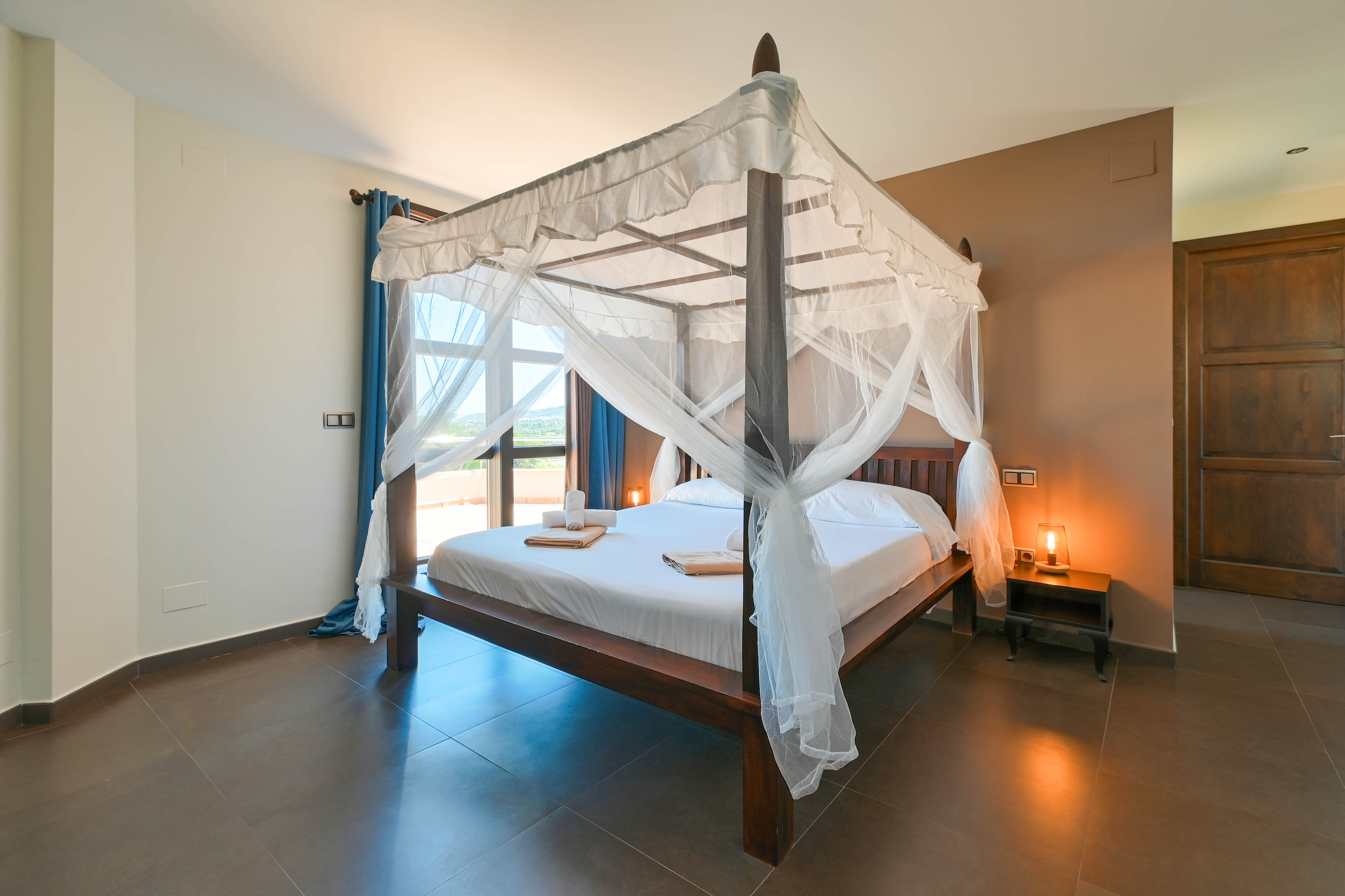Bedroom featuring a dark wood canopy bed with white curtains, and brown tile flooring.