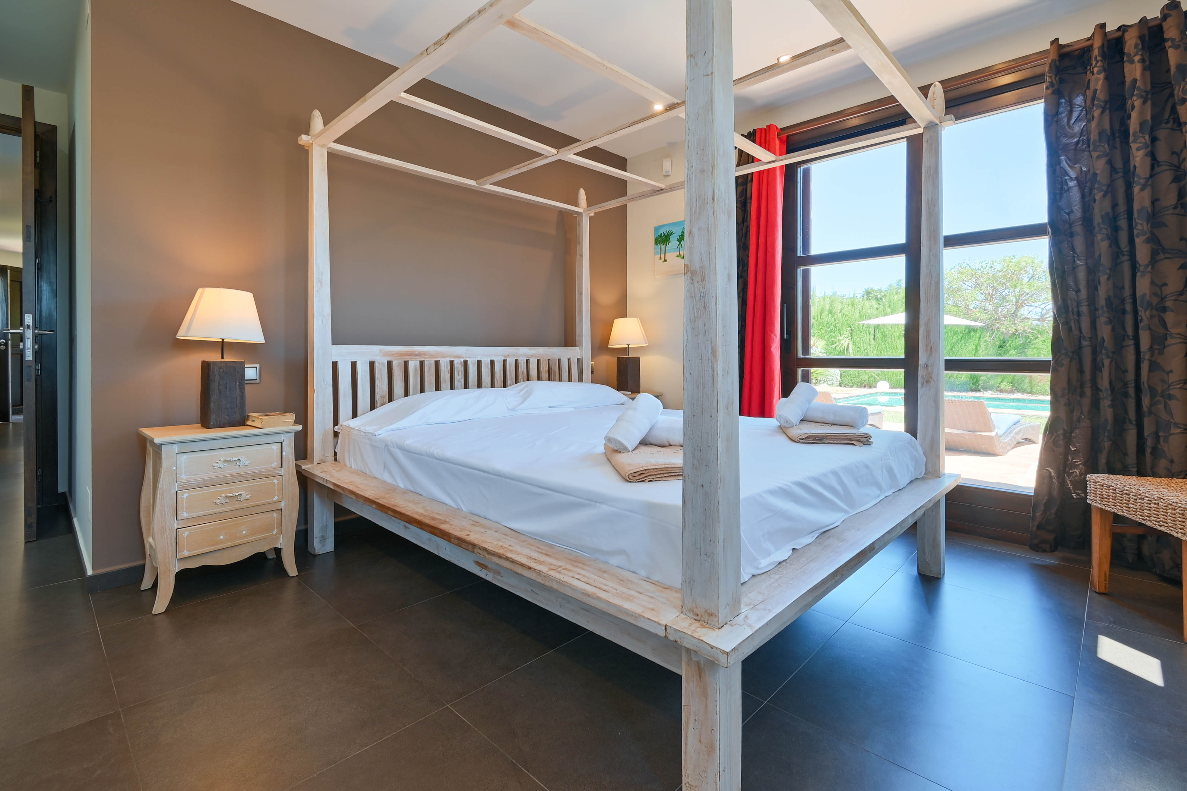 Bedroom featuring a white wooden four-poster bed, rustic nightstand, and views overlooking the pool.