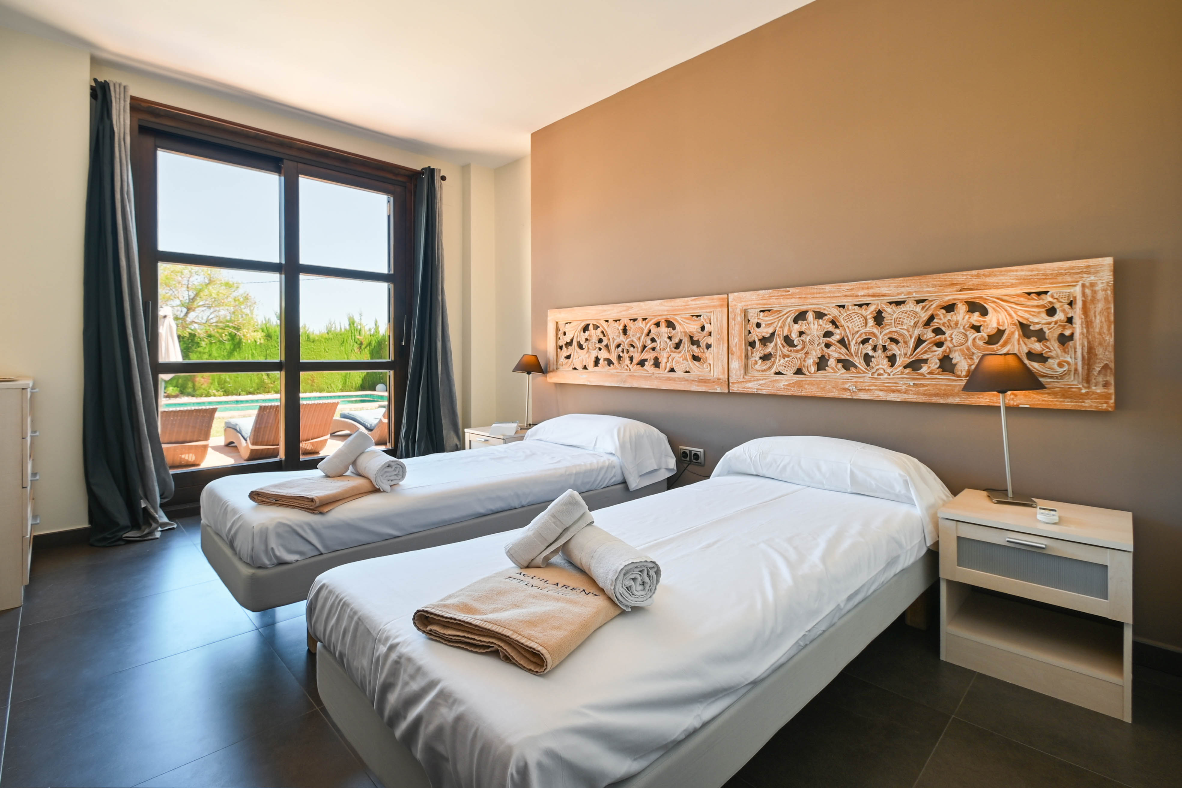 Bright bedroom featuring twin beds, carved wood headboards, and a view overlooking the pool area.