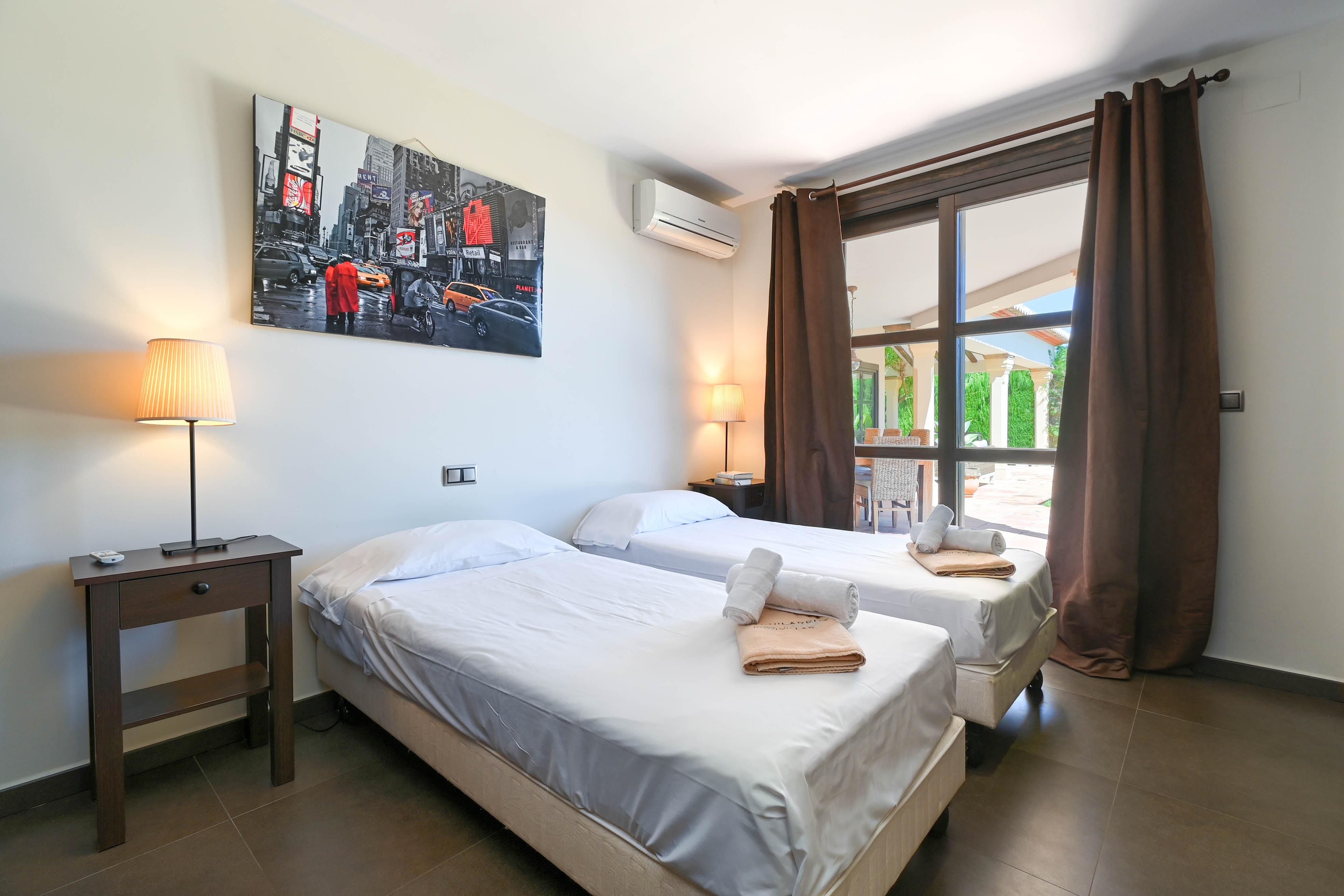 Bright bedroom featuring twin beds, dark wood nightstand, and modern decor with a Times Square print.