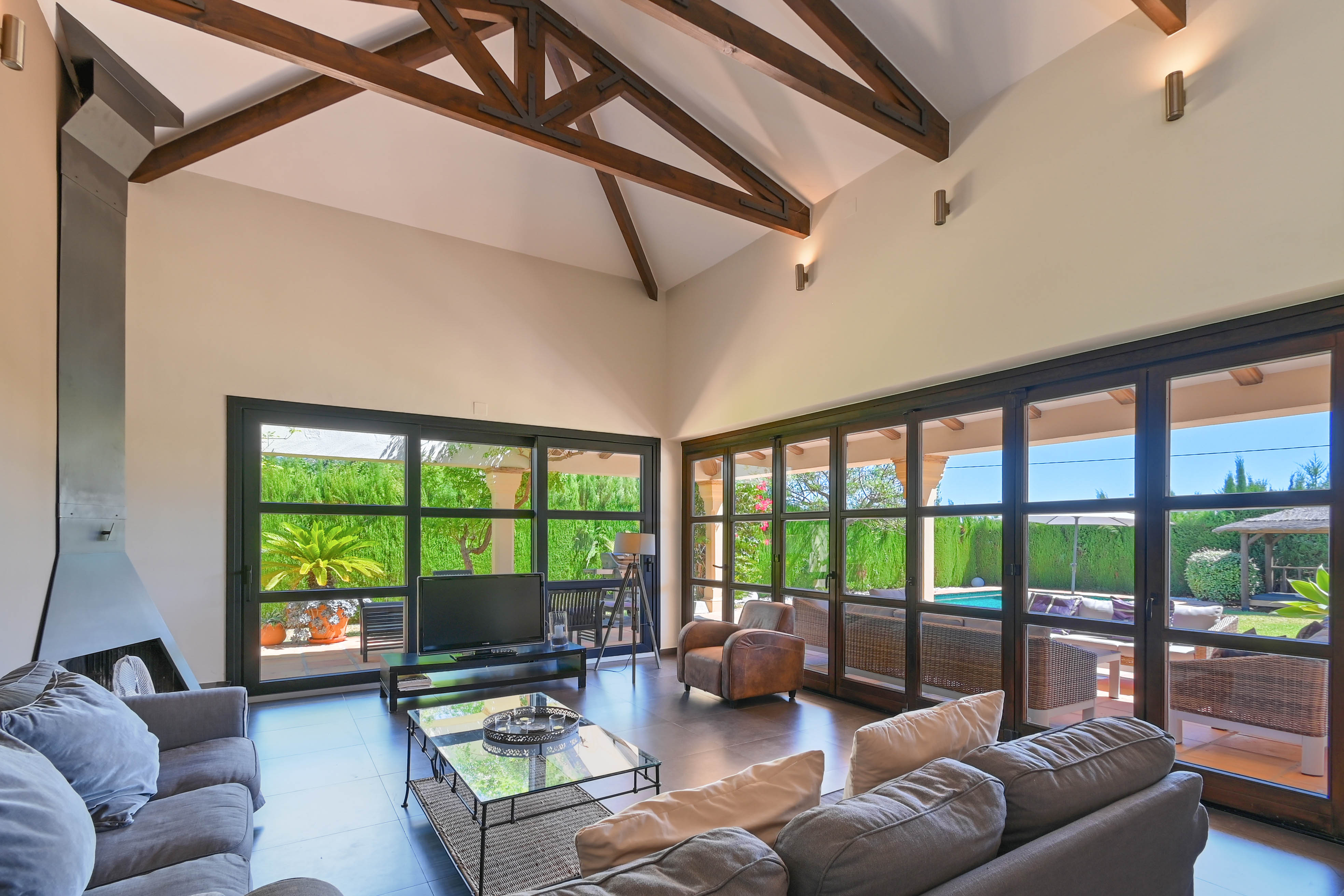Bright living room featuring wood beams, a modern fireplace, and garden views with a pool through expansive windows.