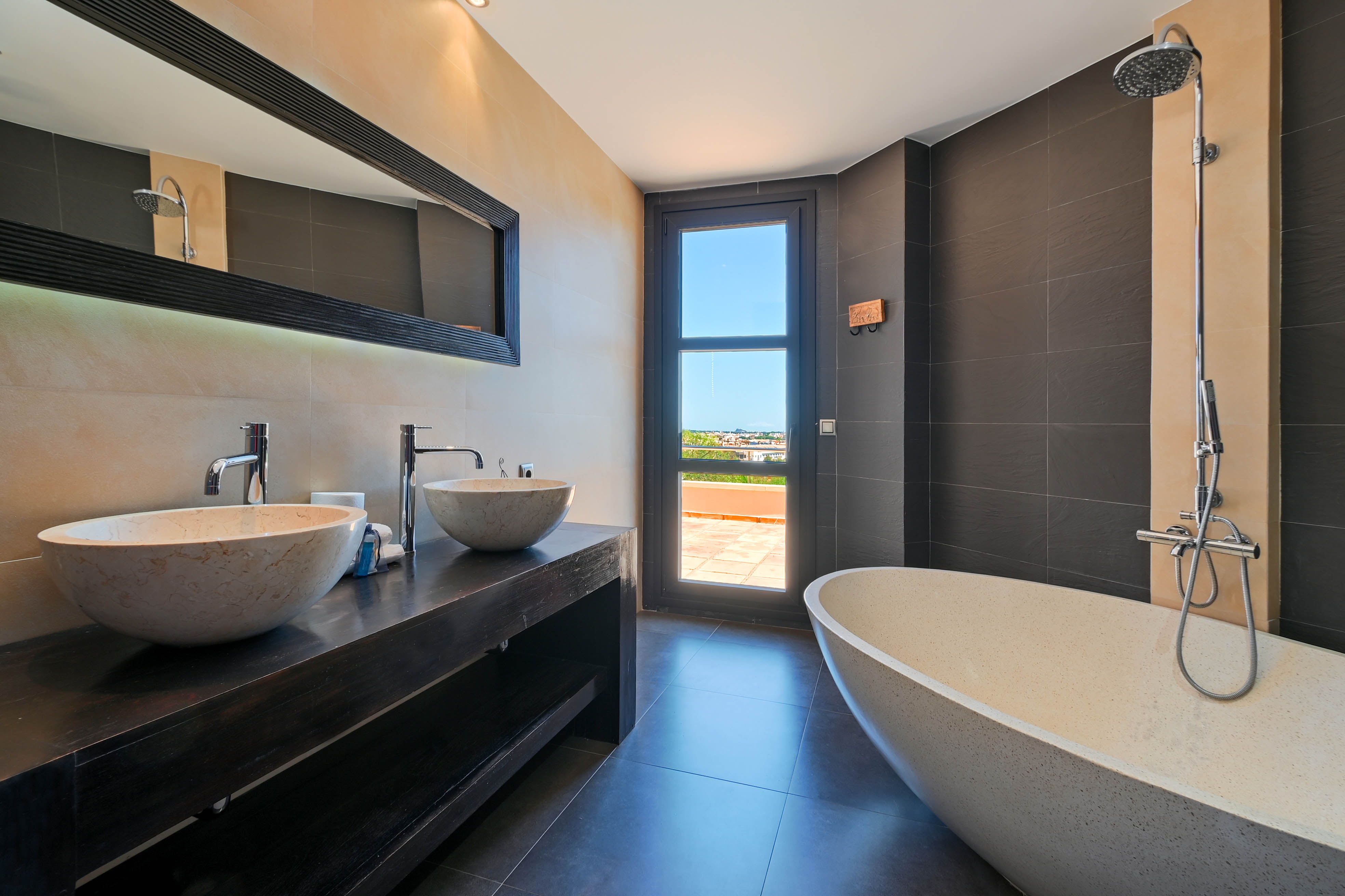 Elegant bathroom with double stone sinks and a freestanding bathtub, with access to an outdoor terrace.