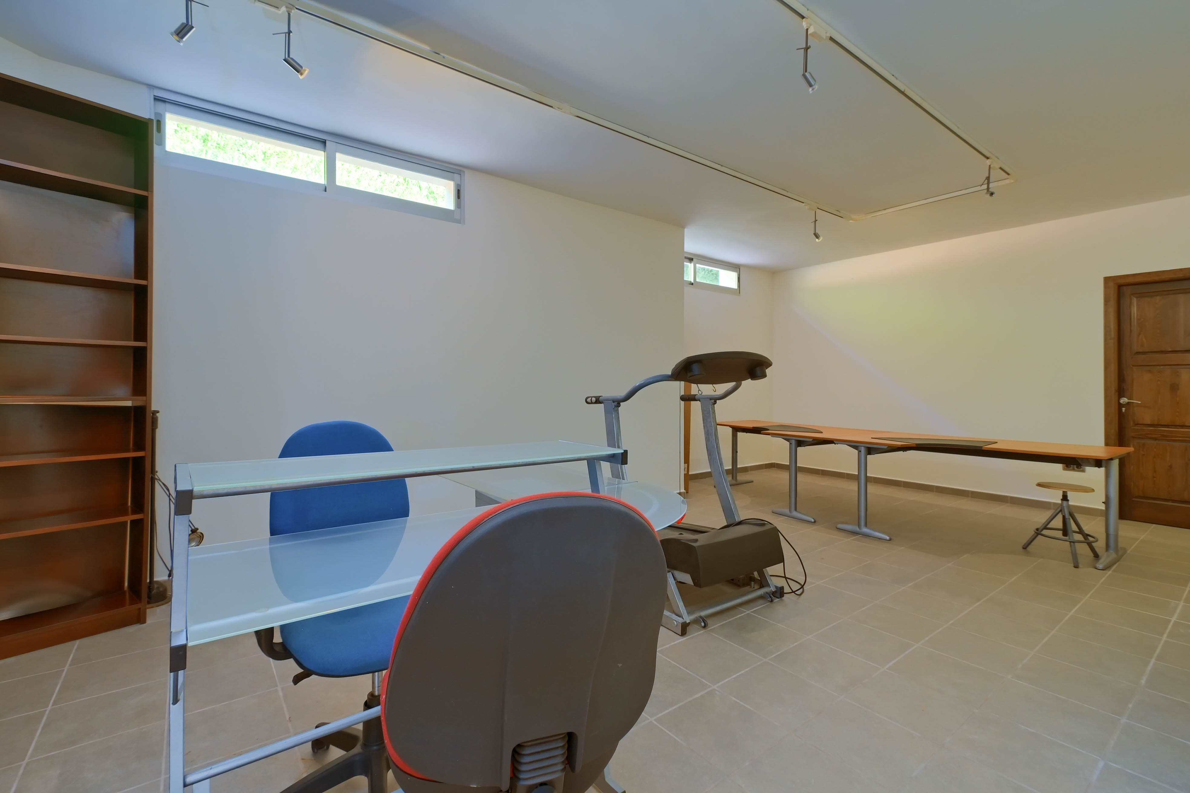 Functional space featuring shelving, glass desk, and treadmill, set on neutral tile flooring.