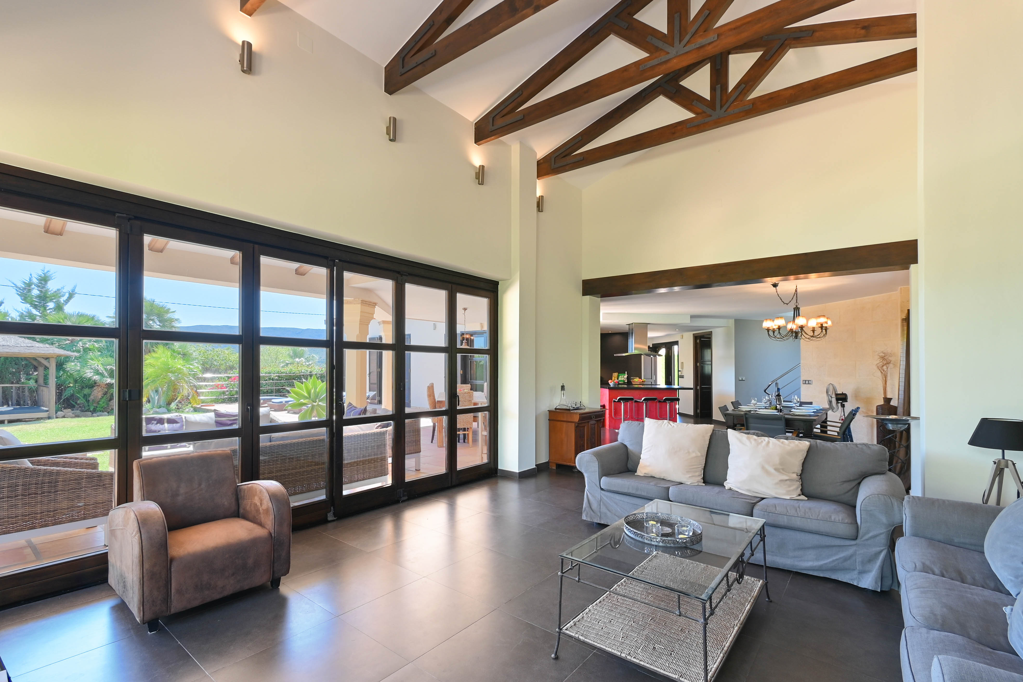 Living room with wood beams, gray sofas, and large windows overlooking the garden.