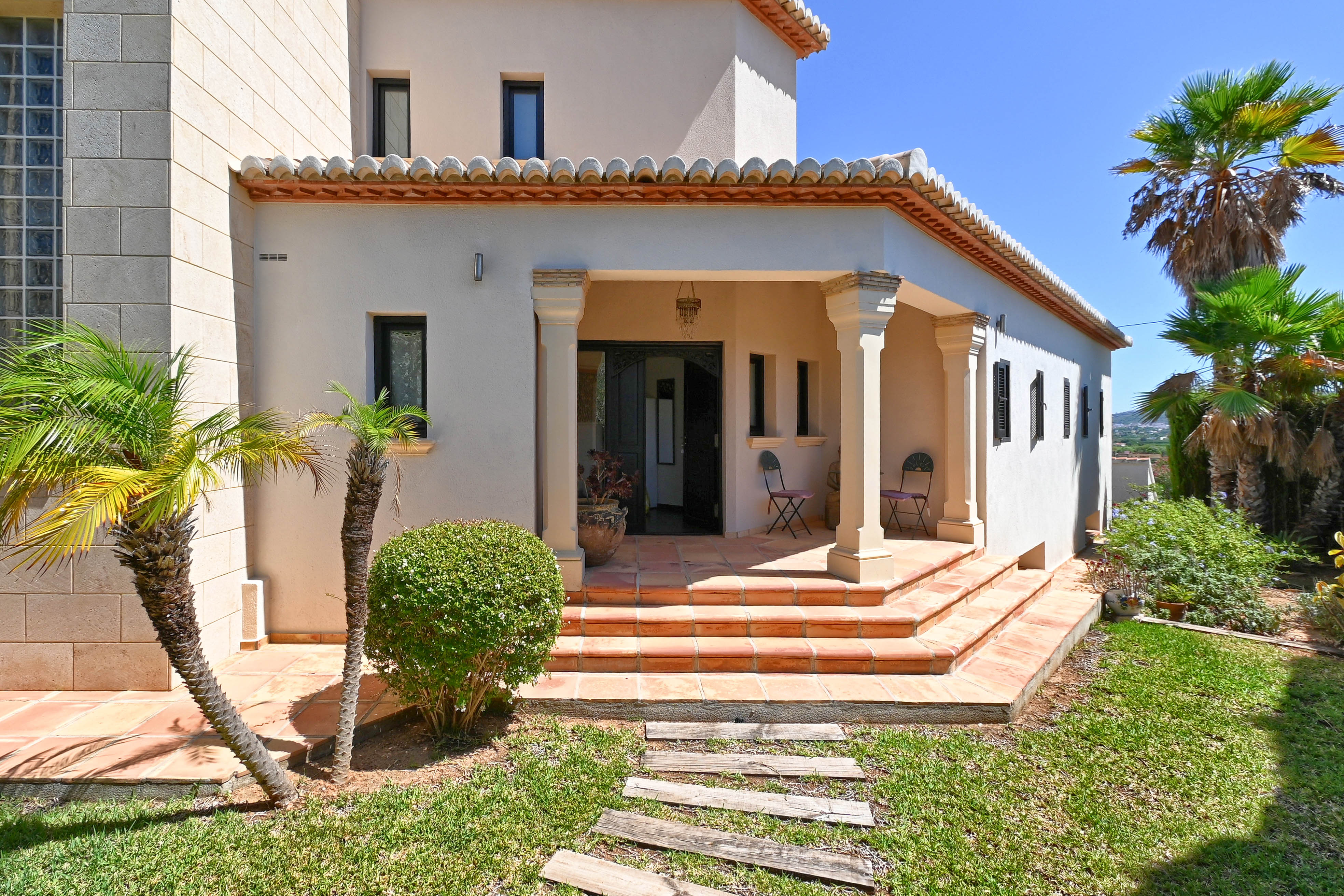Main entrance of the villa featuring terracotta steps and a manicured garden with palm trees.