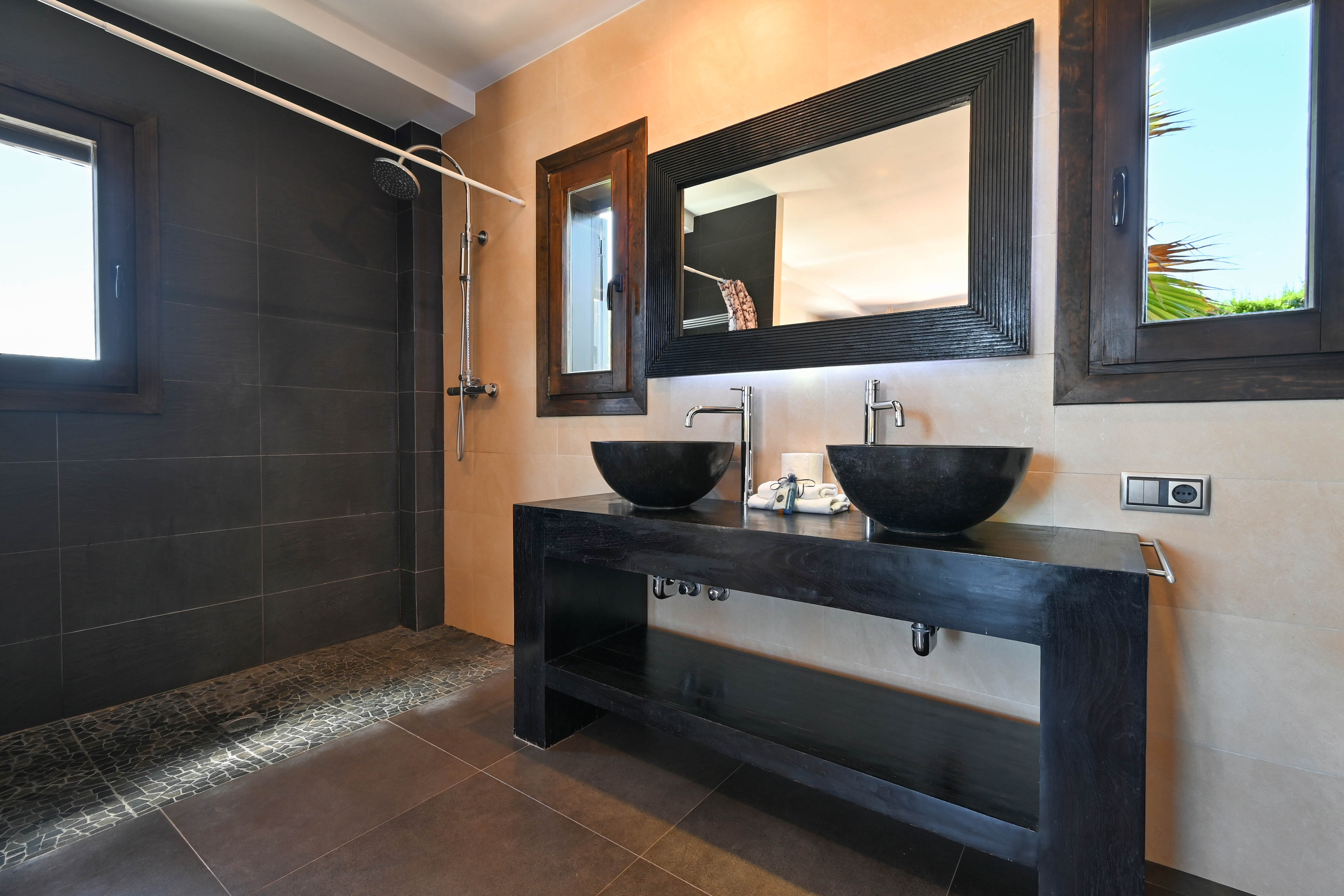 Modern bathroom detail featuring a double stone sink and dark tiled shower area.