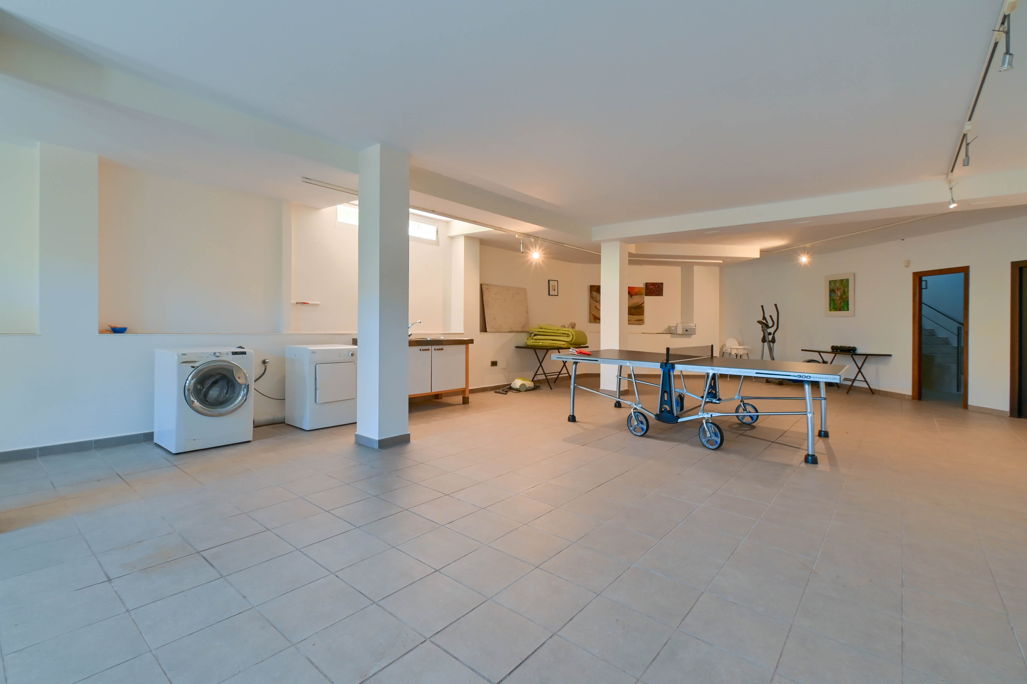 Spacious game room with washer, dryer, and ping-pong table on cream-colored tile flooring.