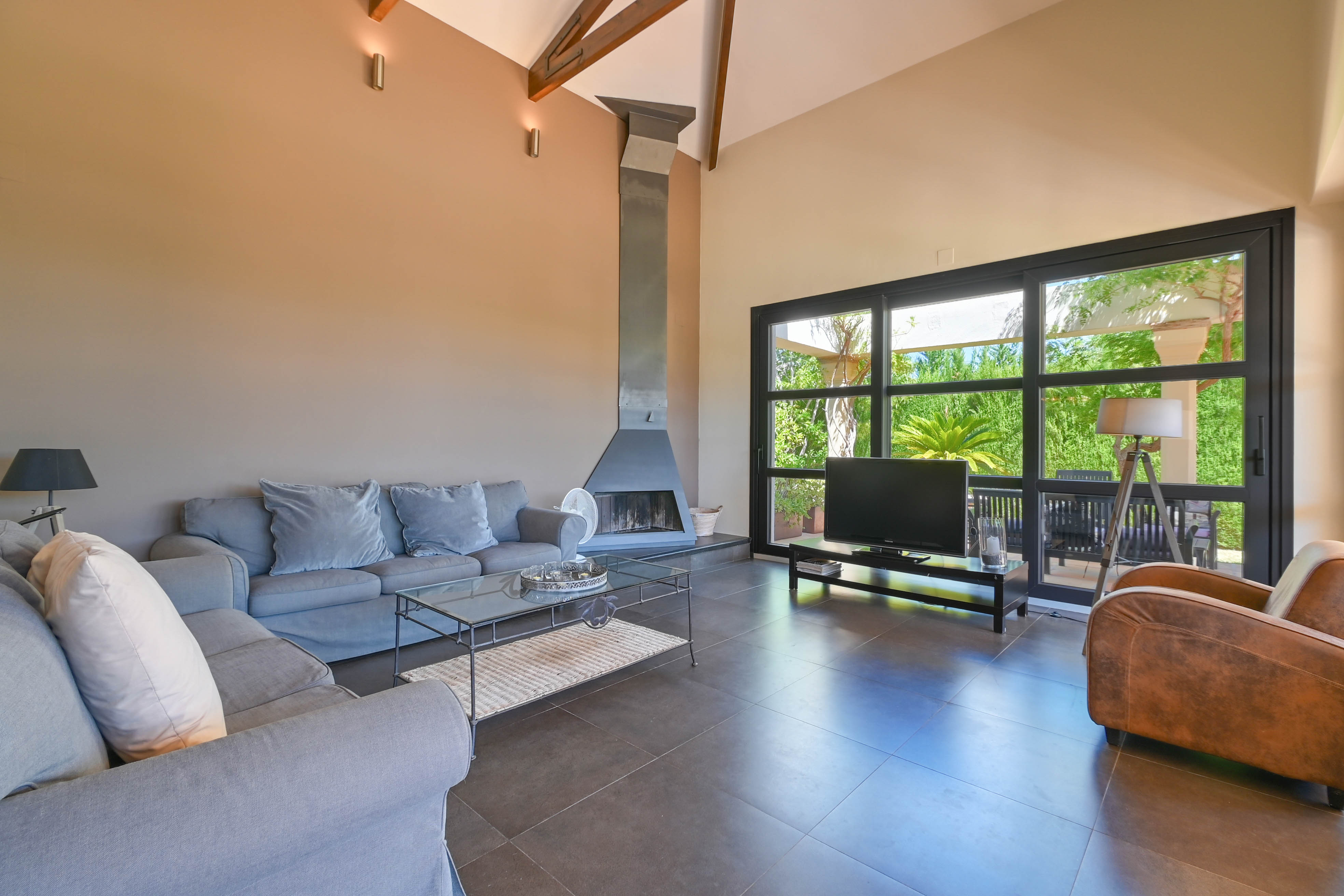 Spacious living room featuring a metal fireplace, gray sofa, and large windows overlooking the garden in Denia, Costa Blanca.