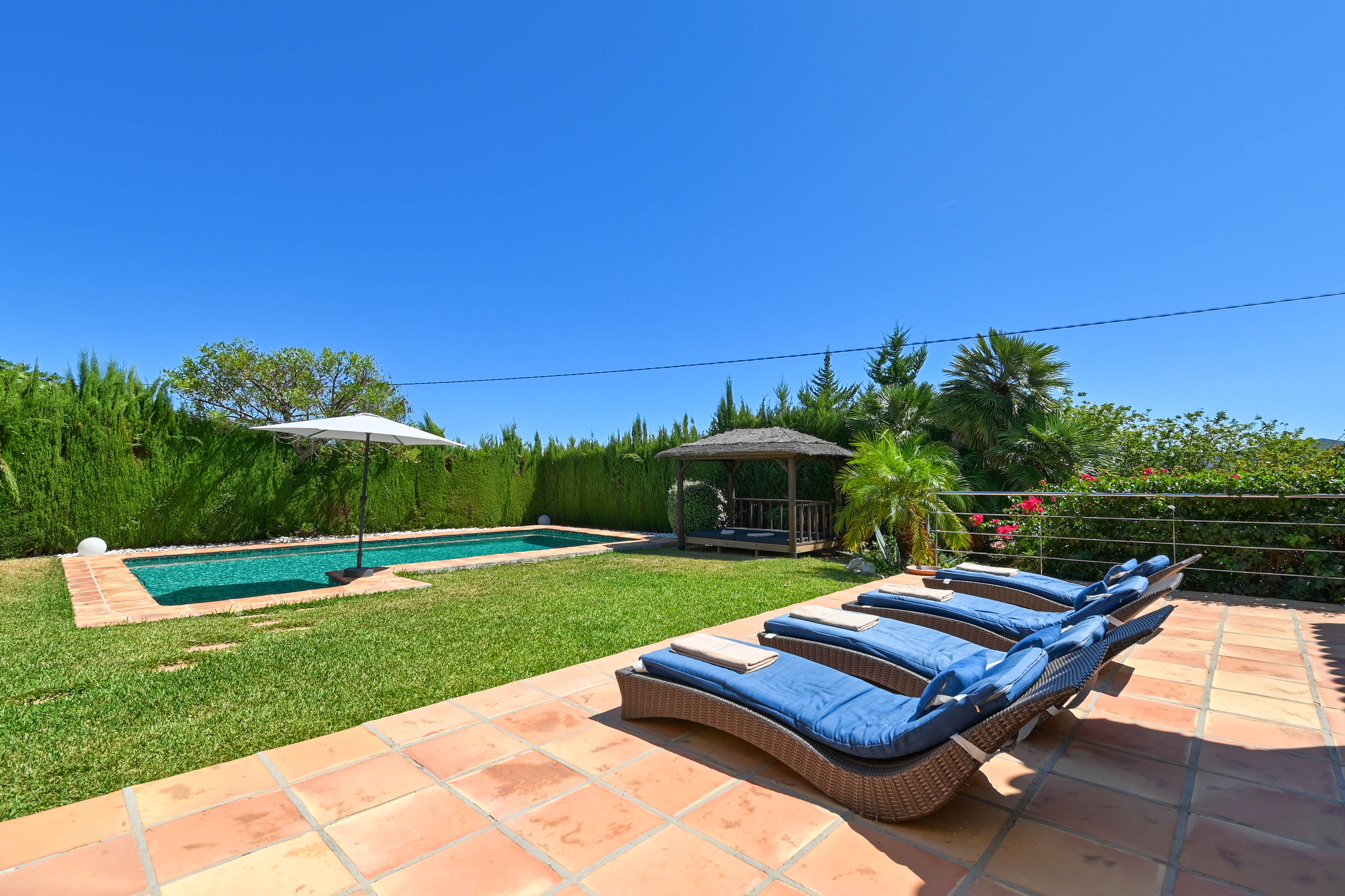 Sun terrace with blue rattan loungers, pool, and gazebo in a landscaped lawn garden.