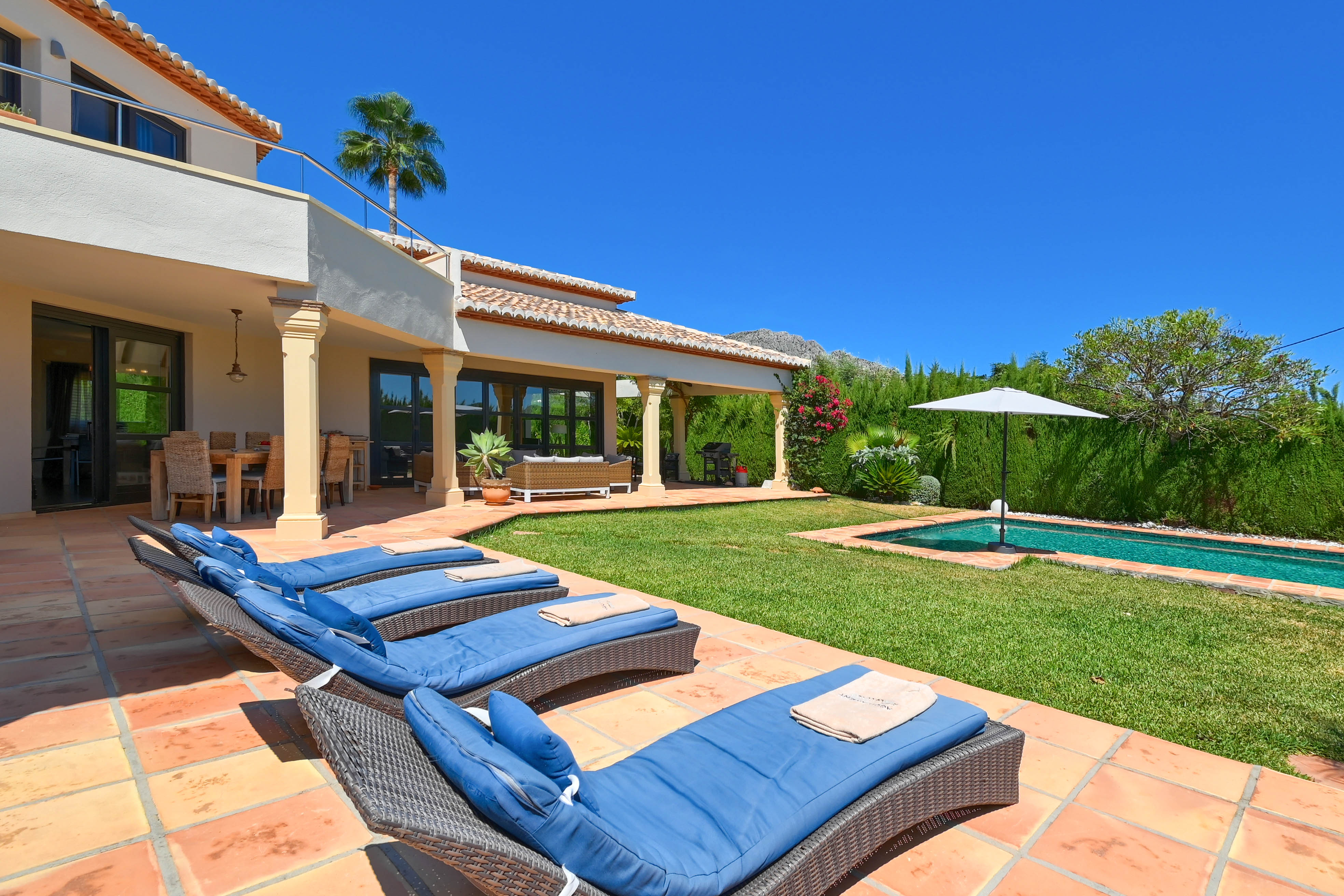Terrace with blue lounge chairs and elongated pool in a grassy garden.