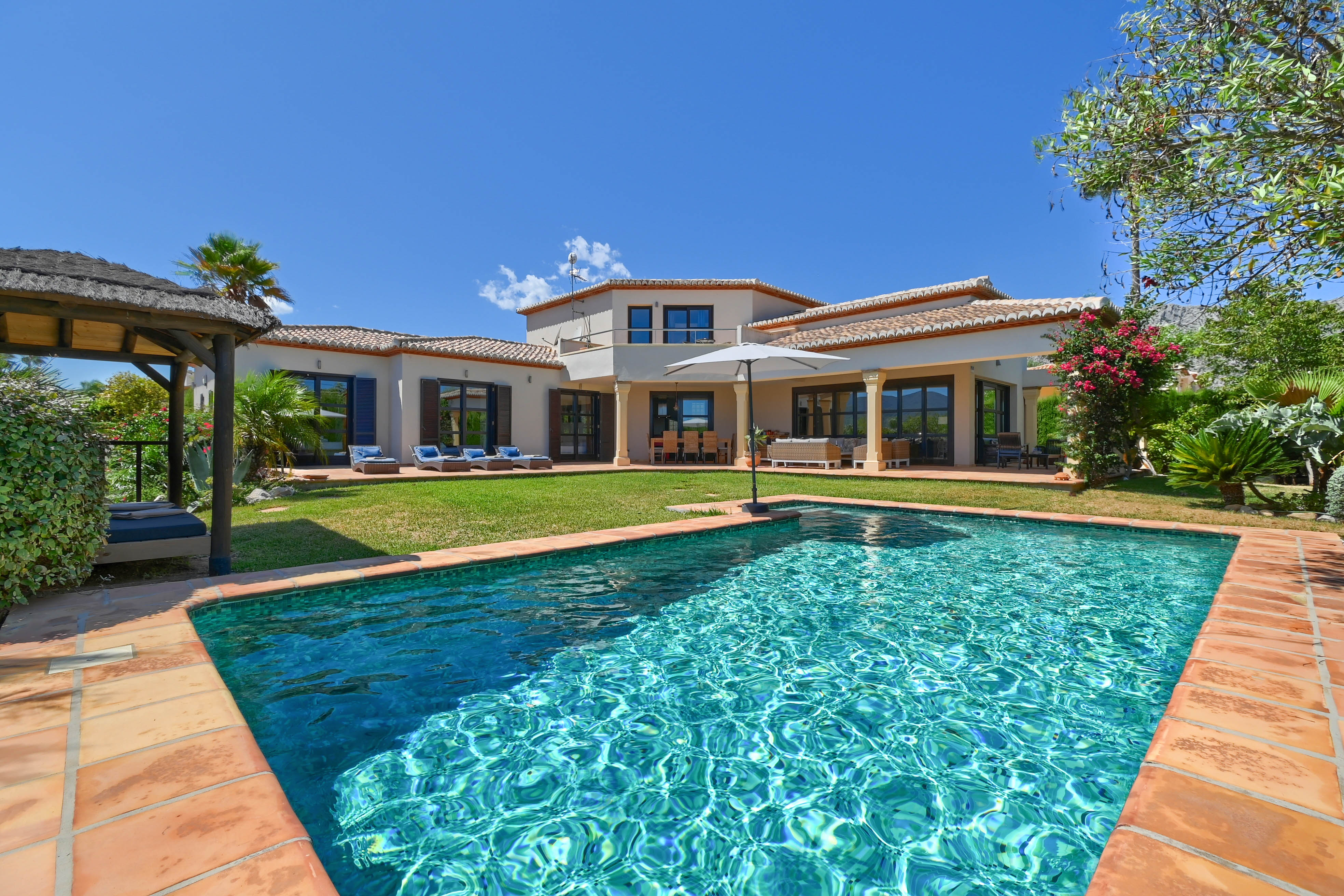 View of the turquoise pool with terracotta trim and the two-story villa with shutters.