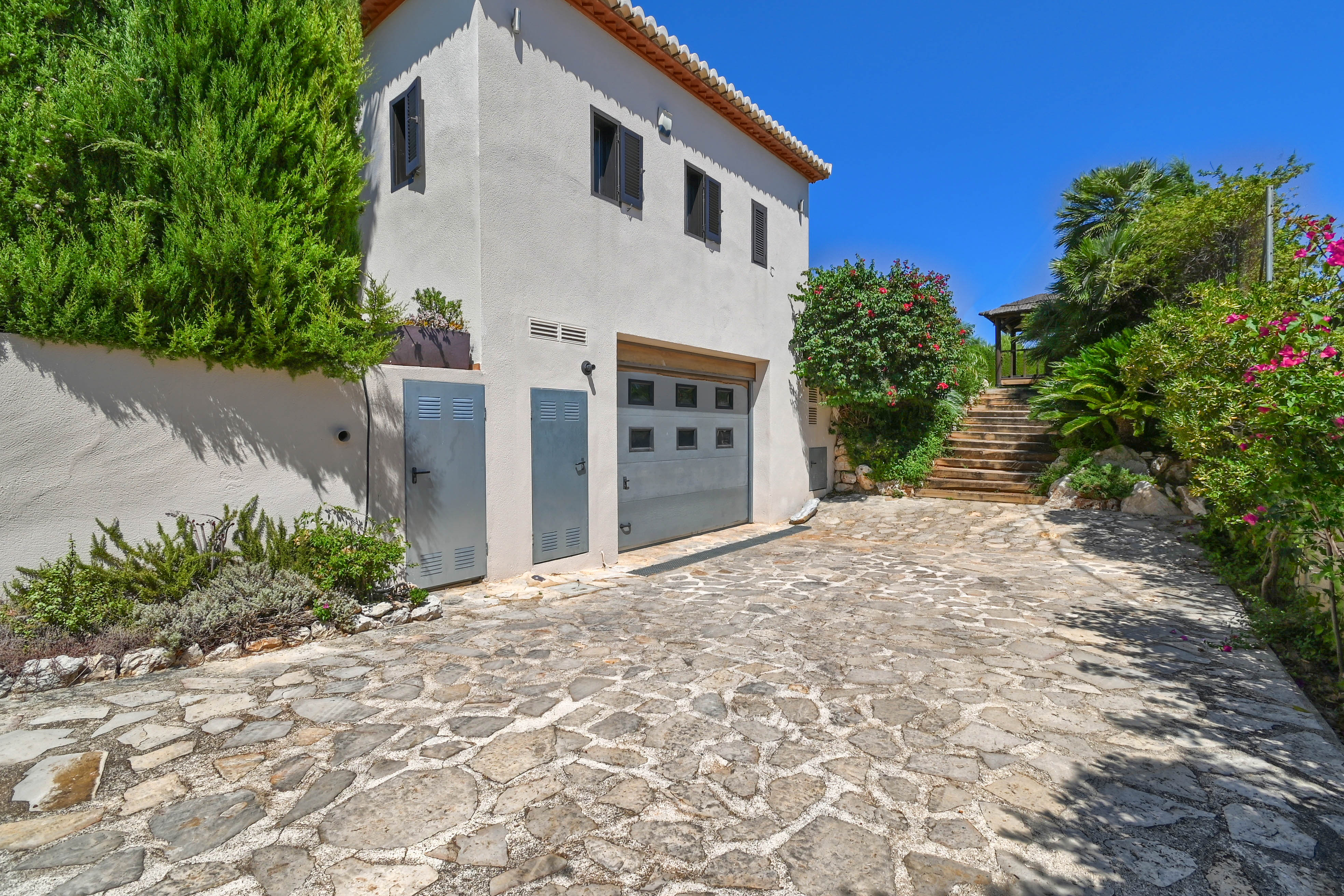 Villa exterior featuring a stone driveway, greenery, and a gray garage.