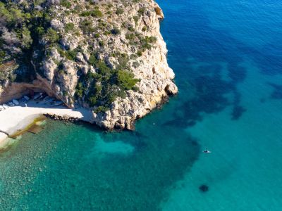 Aerial view of a rocky cove with boats on the beach and turquoise waters.