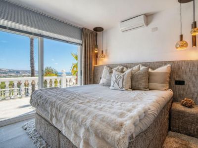 Bright bedroom with terrace access and sea views. Bed features an upholstered headboard and neutral-toned bedding.