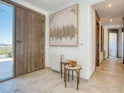 Bright foyer with wooden door and marble floor. Features abstract artwork and side tables.