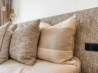 Close-up of the bed featuring a woven textured headboard and decorative pillows in neutral tones. Electrical outlet integrated into the headboard.