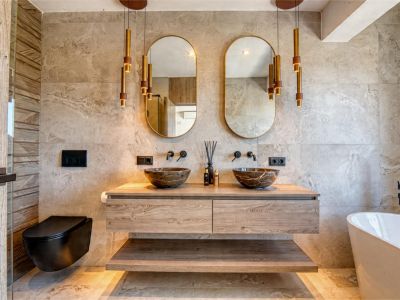 Elegant bathroom featuring stone vessel sinks, floating wood vanity, and gold pendant lights. Modern design with neutral tile.