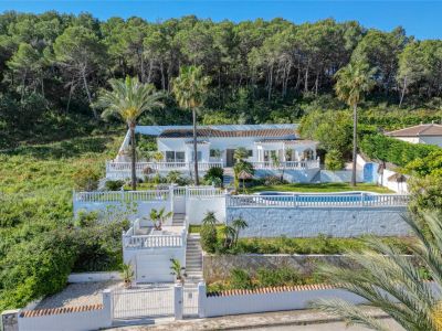 Exterior view of the villa in Piver, Jávea, showcasing its white facade, pool, and terraced gardens with Mediterranean greenery.