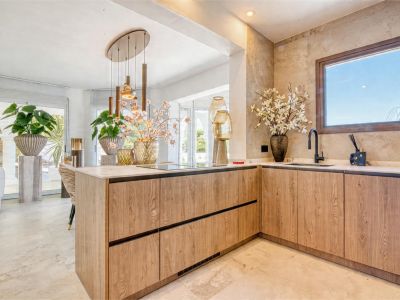 Kitchen detail with light wood central island and marble countertop. Pendant lighting and ornamental plants.