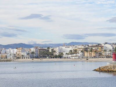 Panoramic view of Jávea's beach and promenade, featuring residential buildings and mountains in the background.