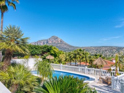 Pool view with blue mosaic tile border, surrounded by lush tropical greenery and white railing.