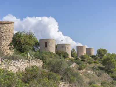 View of historic stone windmills in Jávea, integrated into the Mediterranean landscape.