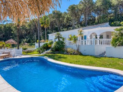 View of the turquoise blue pool with tiled edge, surrounded by lawn and lush greenery, with the white villa in the background.