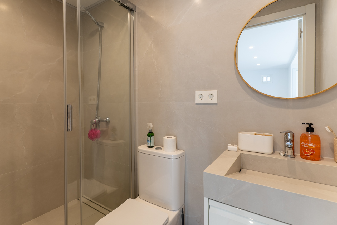 Bathroom detail with glass shower, modern sink, and circular mirror with gold frame.