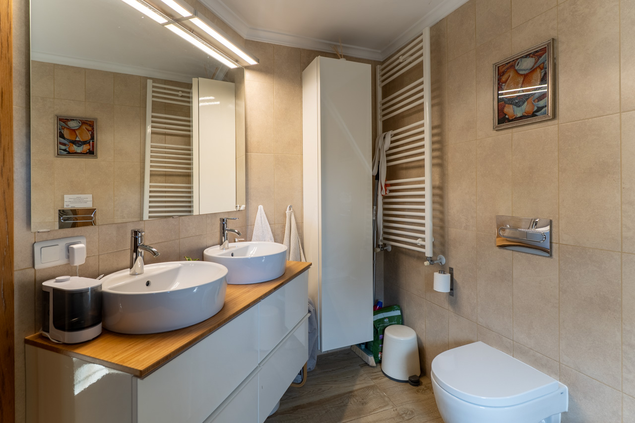 Bathroom featuring double vessel sinks on a wood countertop, a heated towel rack, and sand-toned ceramic tiles.