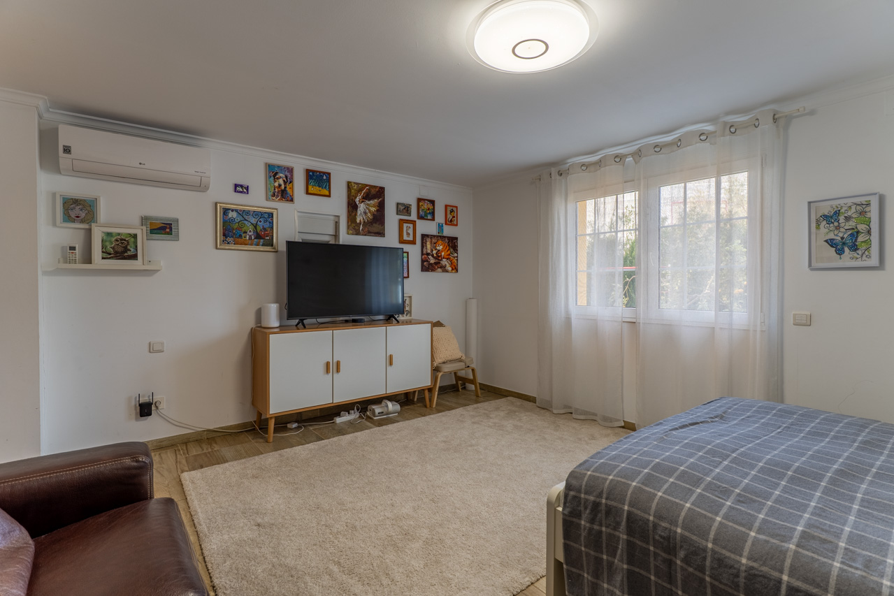 Bright bedroom featuring a plush rug, white TV cabinet, and an eclectic art display on the wall.
