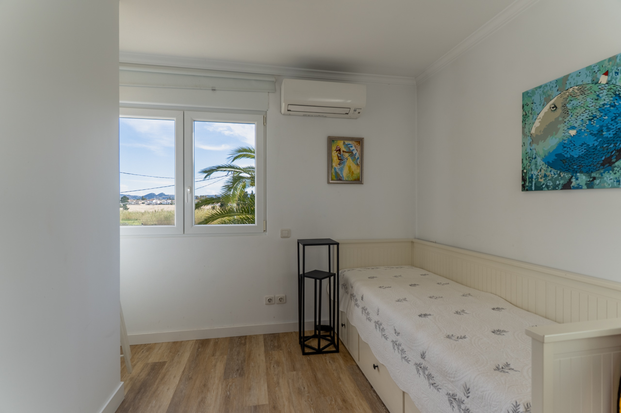 Bright bedroom featuring a single bed, modern decor, and an exterior view with palm trees.