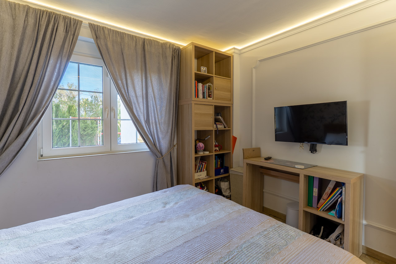 Bright bedroom featuring light wood shelving and grey curtains beside a window.