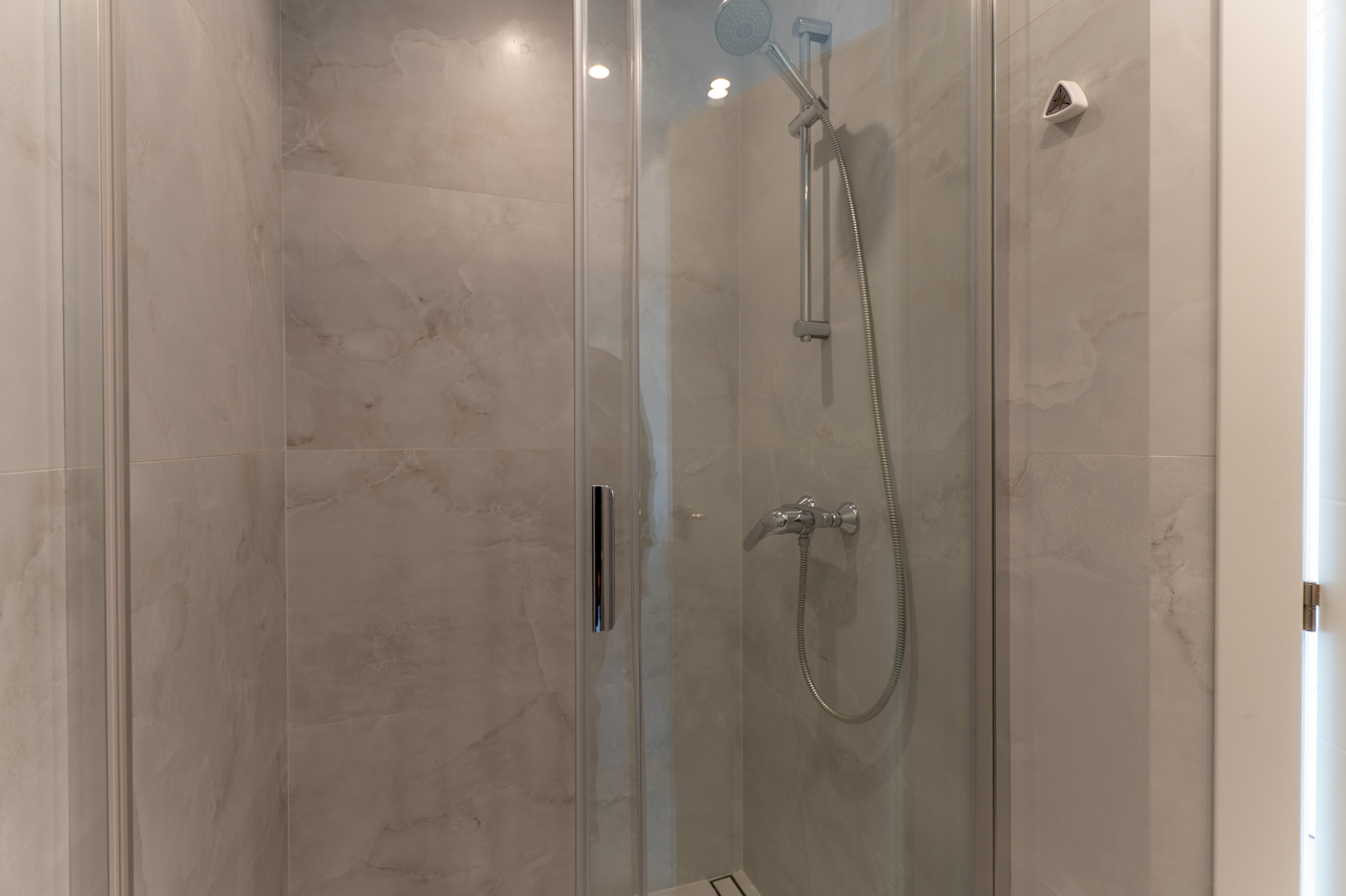 Close-up of the shower featuring a glass screen and marble-effect ceramic tiling.