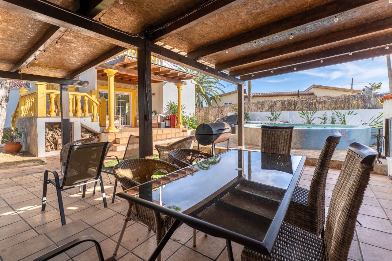 Covered outdoor dining area with barbecue and pool in the villa's garden.
