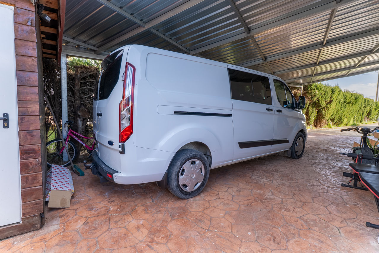 Covered parking area featuring a white van and stamped stone flooring.