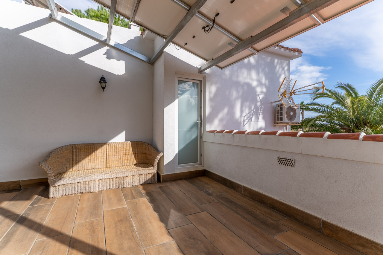 Covered terrace with ceramic flooring and wicker sofa, illuminated by natural light and with outdoor access.
