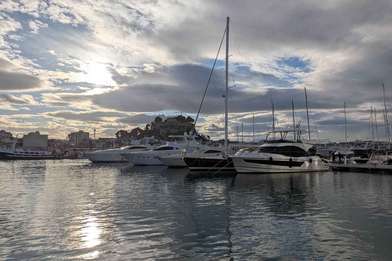 Marina view featuring yachts and sun reflections on the water.