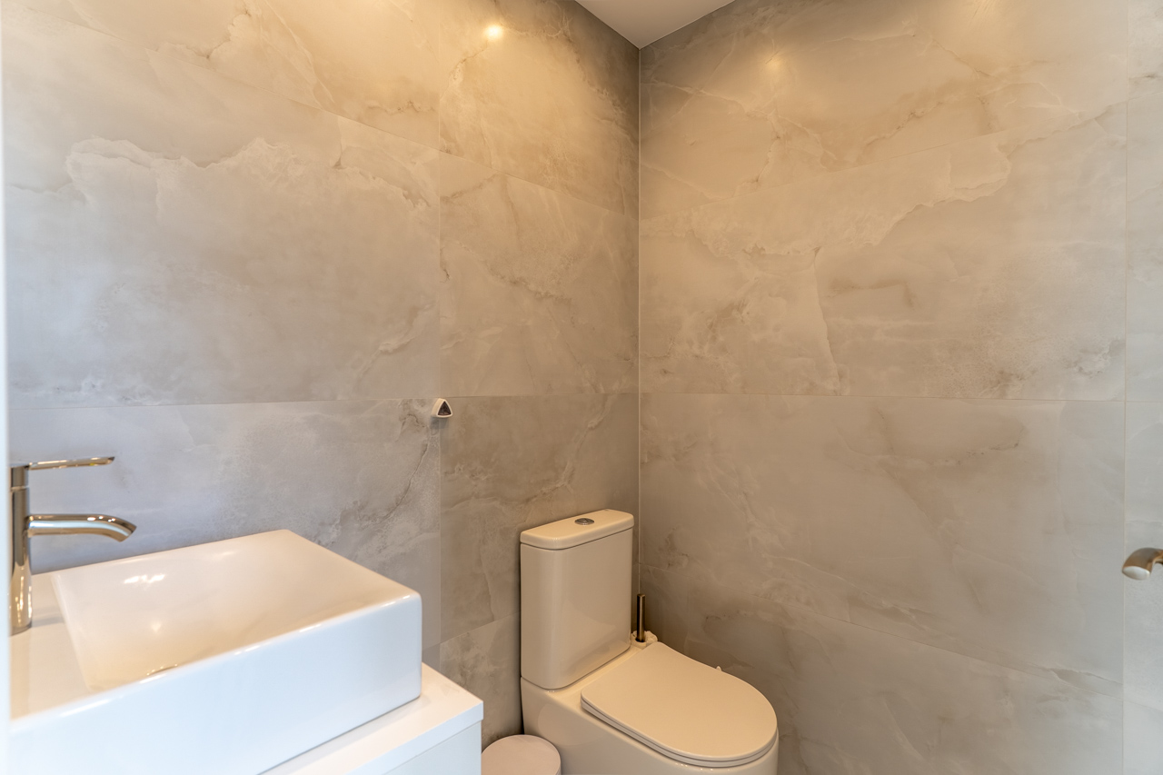 Modern bathroom detail with veined tile walls, a square vessel sink on a white counter, and contemporary toilet.