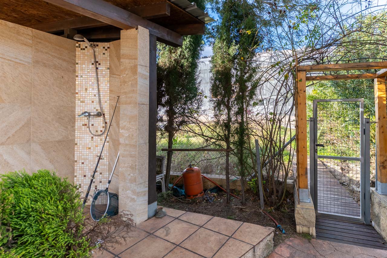 Outdoor shower detail with ceramic cladding and garden area with metal gate.