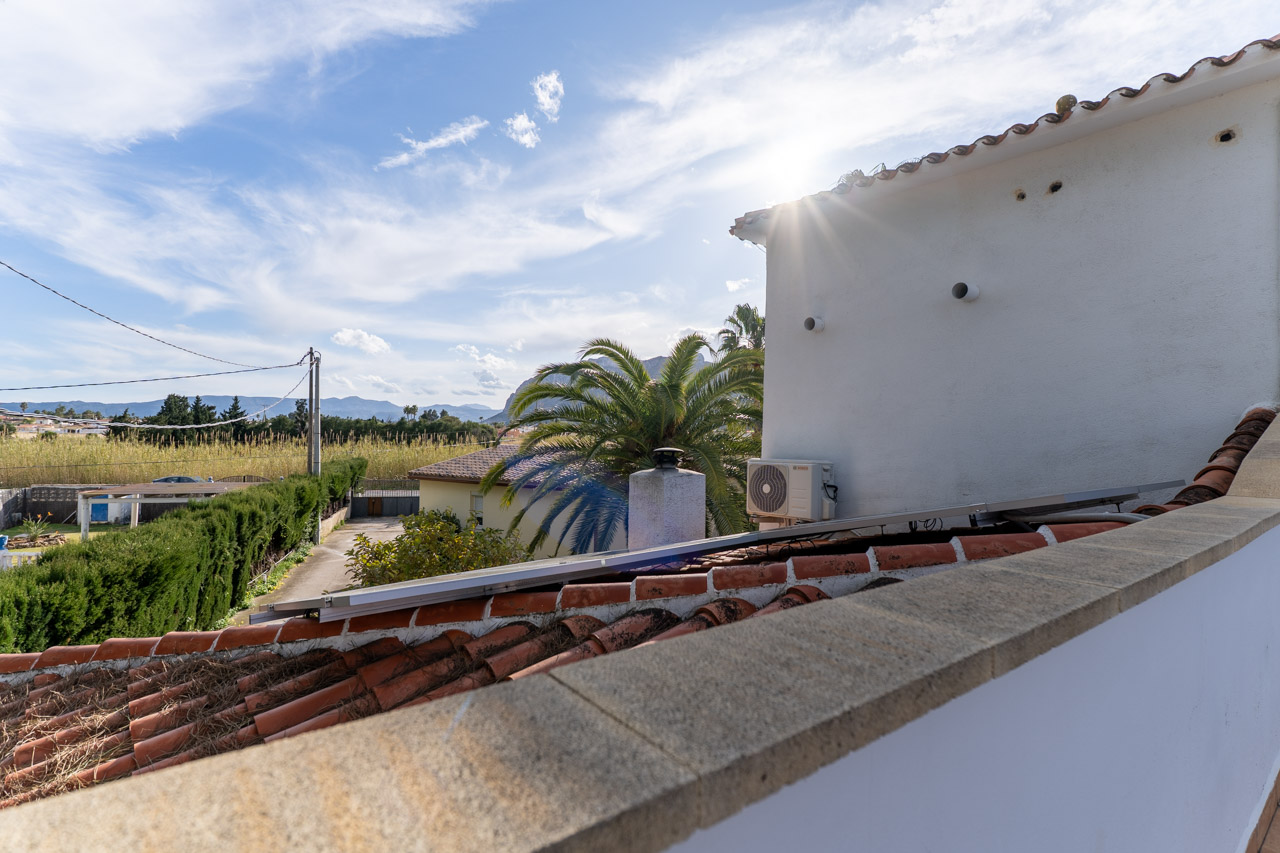 Rooftop view featuring clay tiles and a solar panel. In the background, vegetation and mountains.