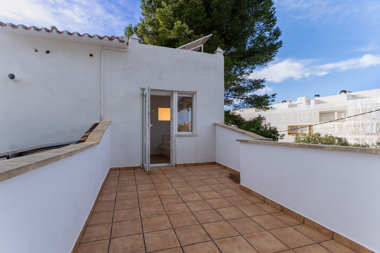 Tiled terrace with white walls. Open door to a bright bedroom.