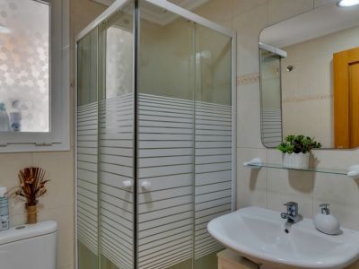 Bathroom detail with corner shower cabin and white sink with rectangular mirror.