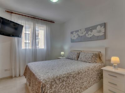 Bright bedroom with double bed, white nightstands, and wall-mounted TV.