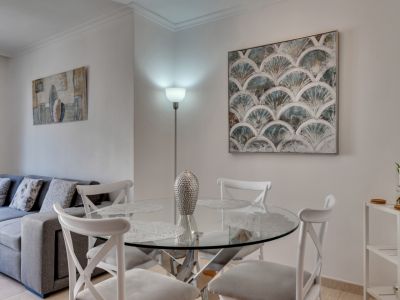 Bright dining area featuring a round glass table with white chairs, complemented by modern art and a floor lamp.