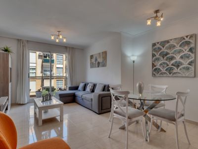 Bright living-dining area with a glass table, gray sectional sofa, and balcony access with urban views.