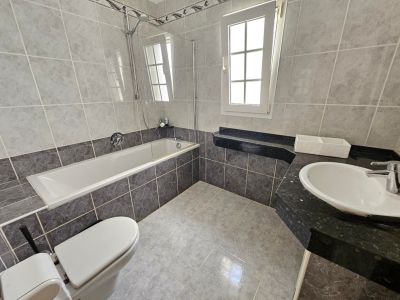 Bathroom featuring gray tile, a bathtub with a glass screen, and a black granite countertop.