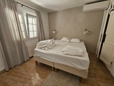 Bedroom featuring a double bed, linen curtains, and rustic tile flooring.